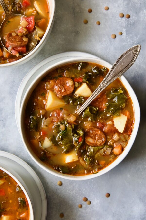 One serving of Spanish Lentil Potato Soup in white bowl with soup spoon with lentils scattered about.