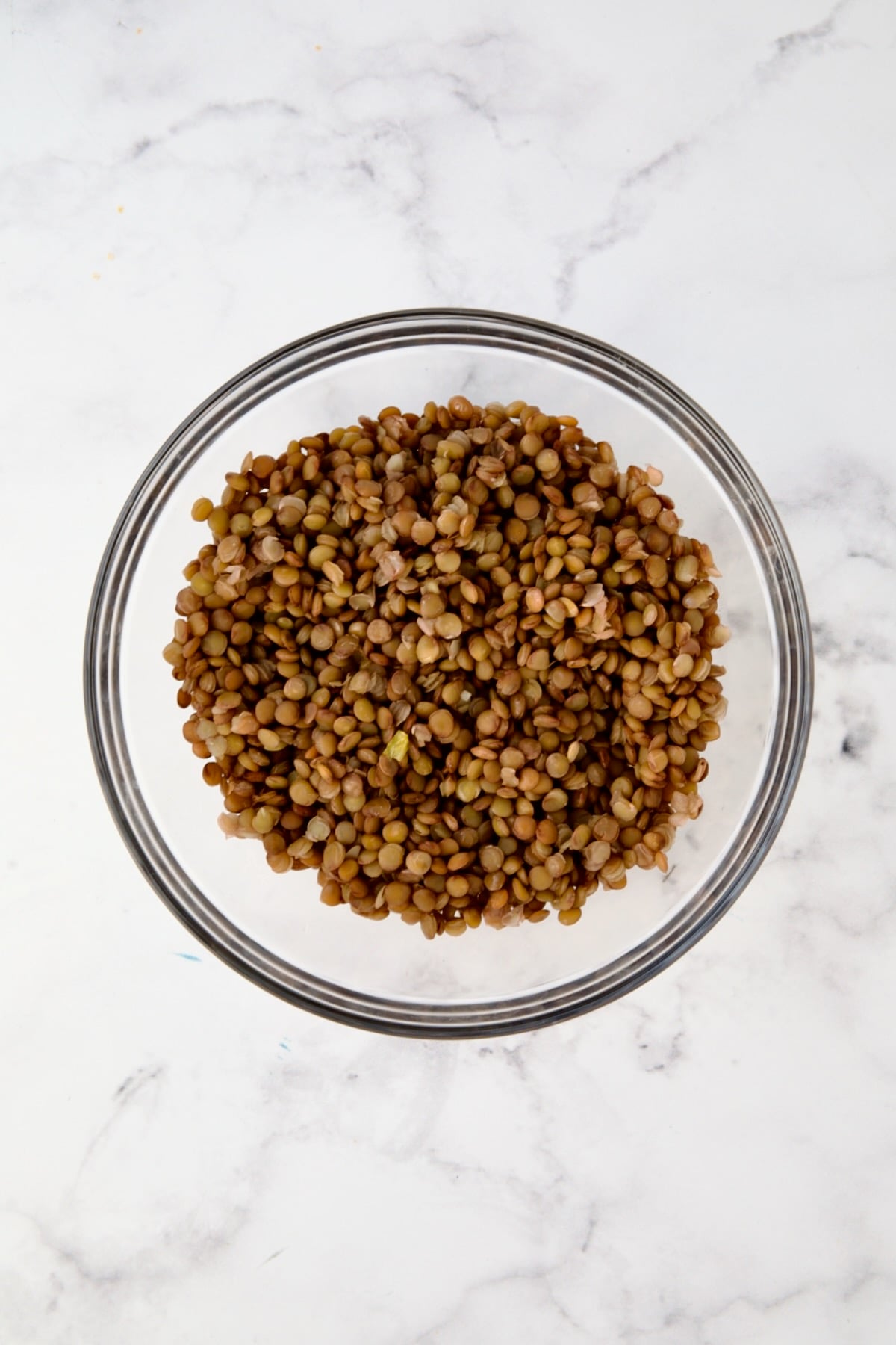 Cooked brown lentils in glass bowl.
