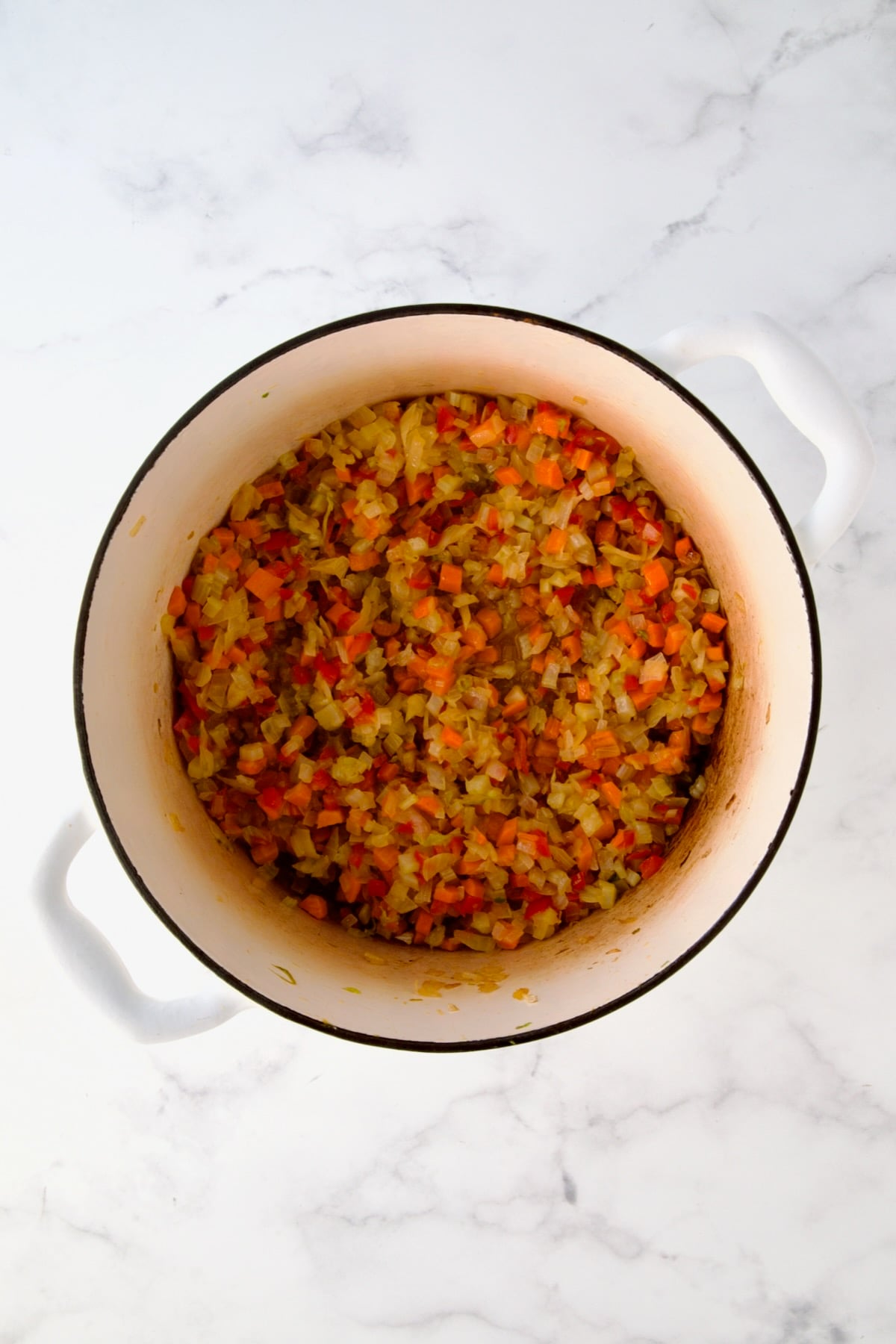 Cooked onions, celery, red bell pepper and carrots in white enamel Dutch oven.