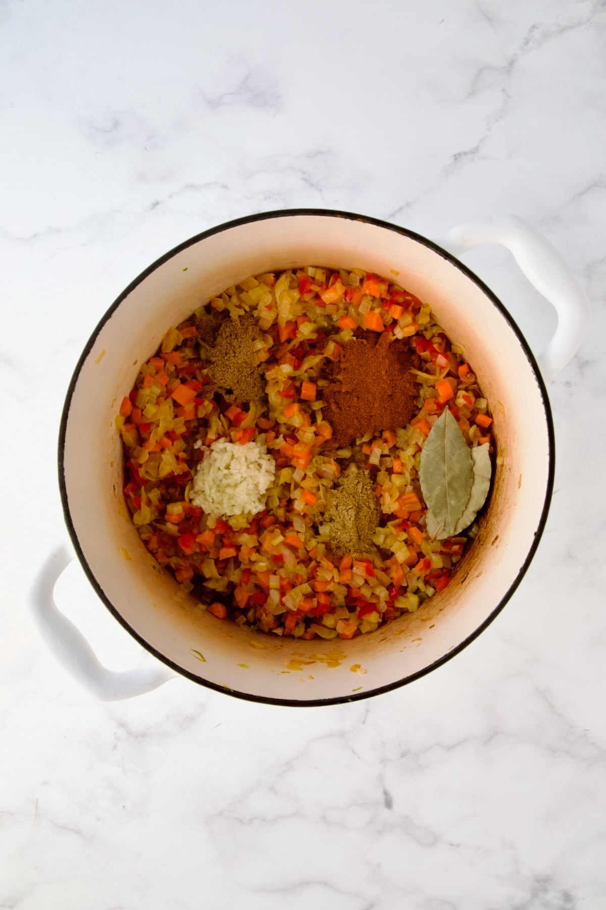 Cooked onions, celery, red bell pepper and carrots in white enamel Dutch oven with herbs and spices added.
