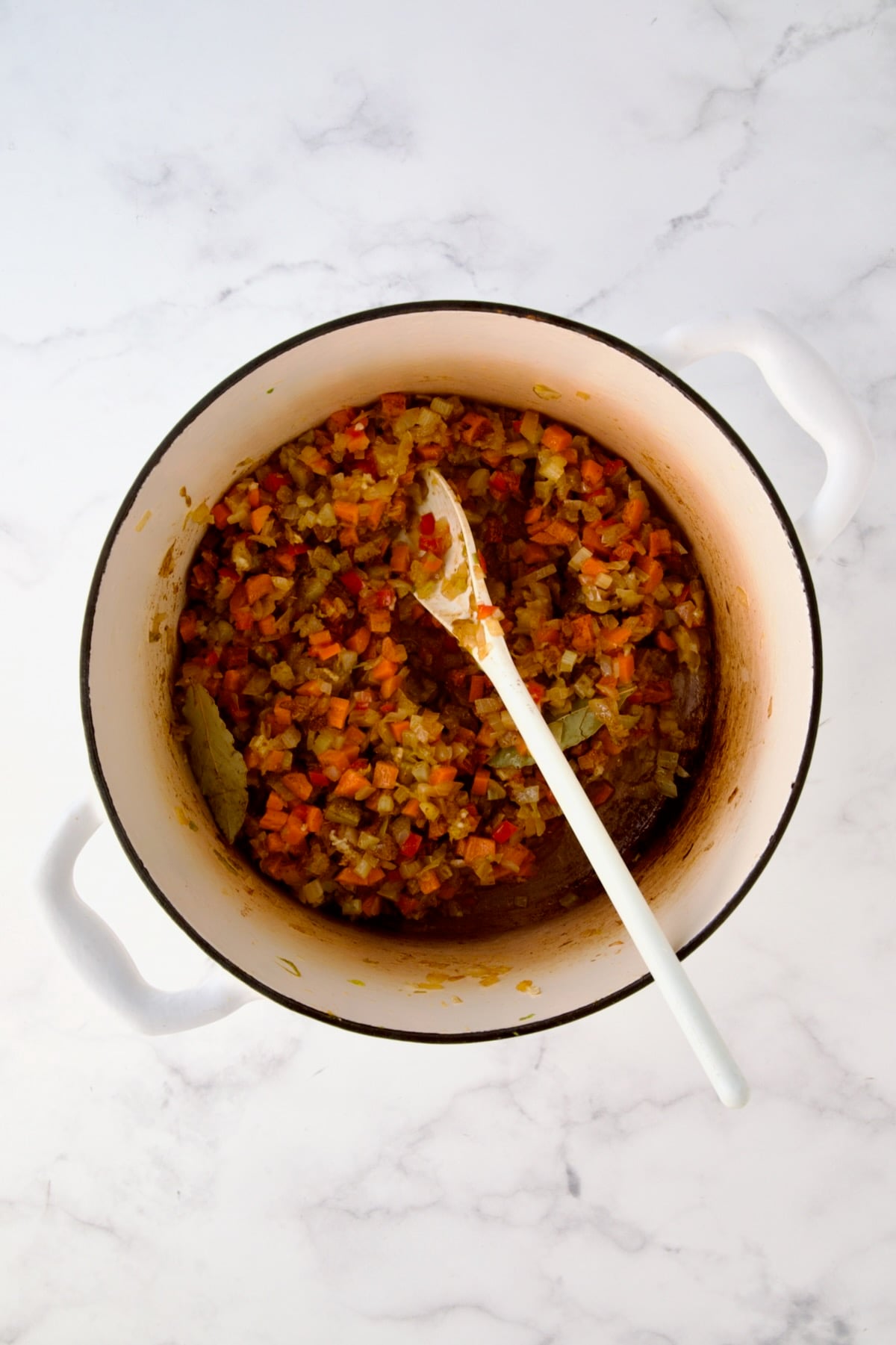 Cooked onions, celery, red bell pepper and carrots in white enamel Dutch oven with herbs and spices stirred in.