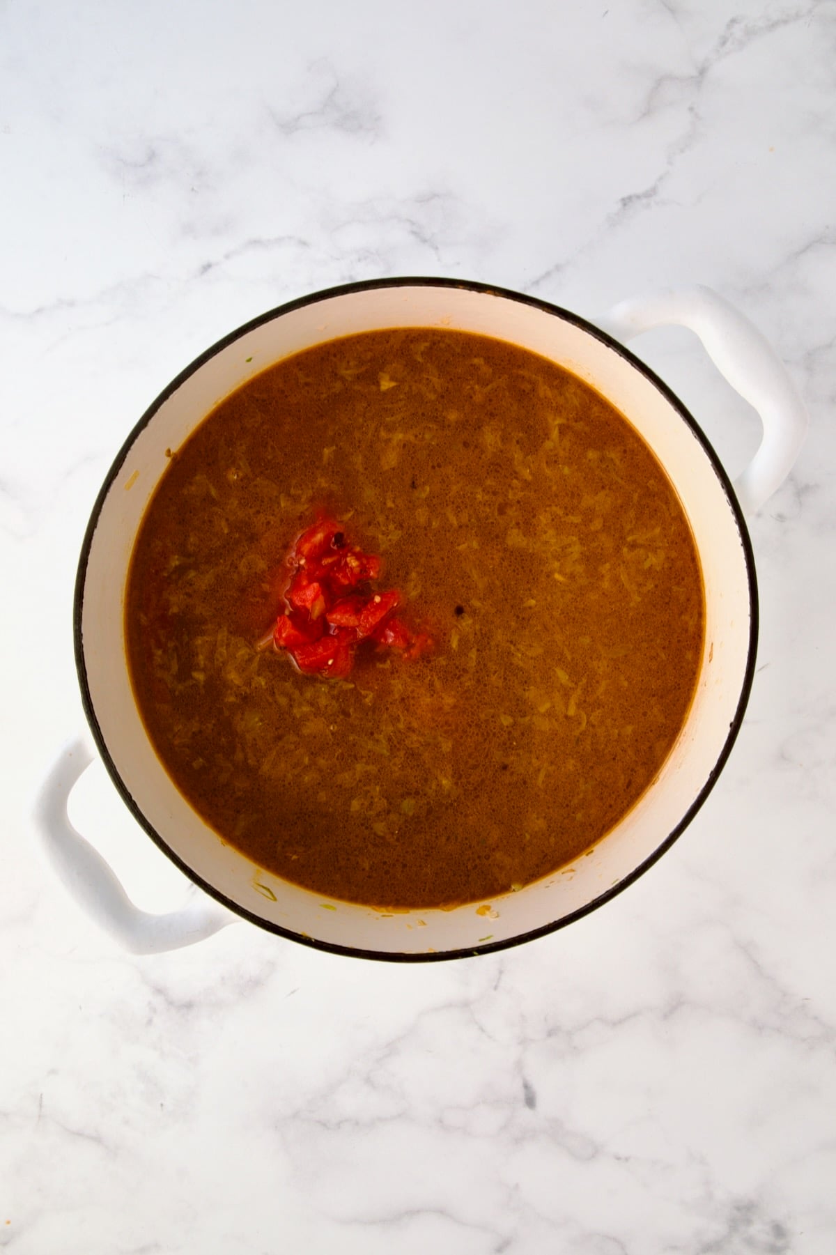 Liquid ingredients added to vegetables in white enamel Dutch oven.