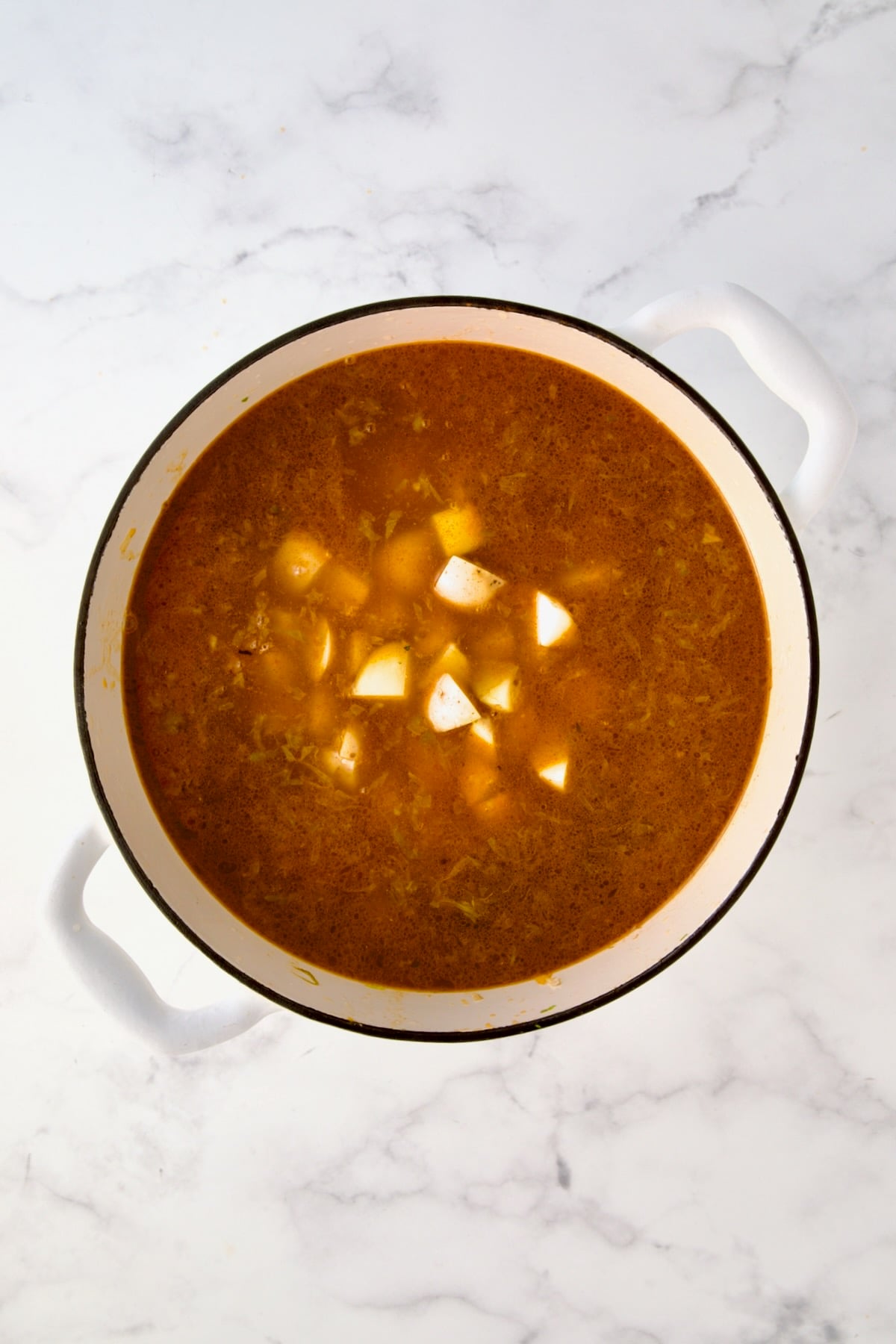 Potatoes added to liquid ingredients in white enamel cast iron Dutch oven.