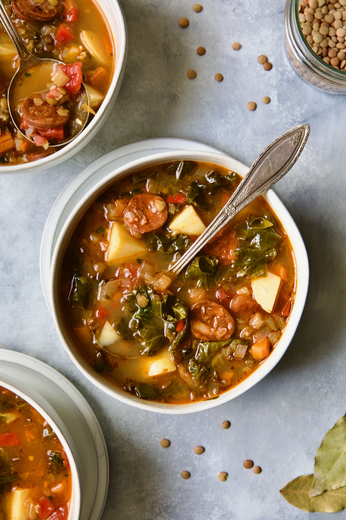 One serving of Spanish Lentil Potato Soup in white bowl with soup spoon.