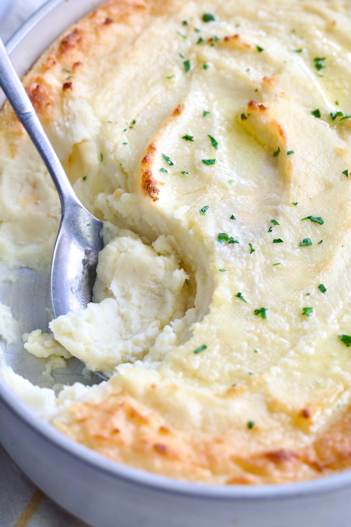 Twice-Baked Mashed Potatoes in white oval baking dish with serving spoon scooping some out.