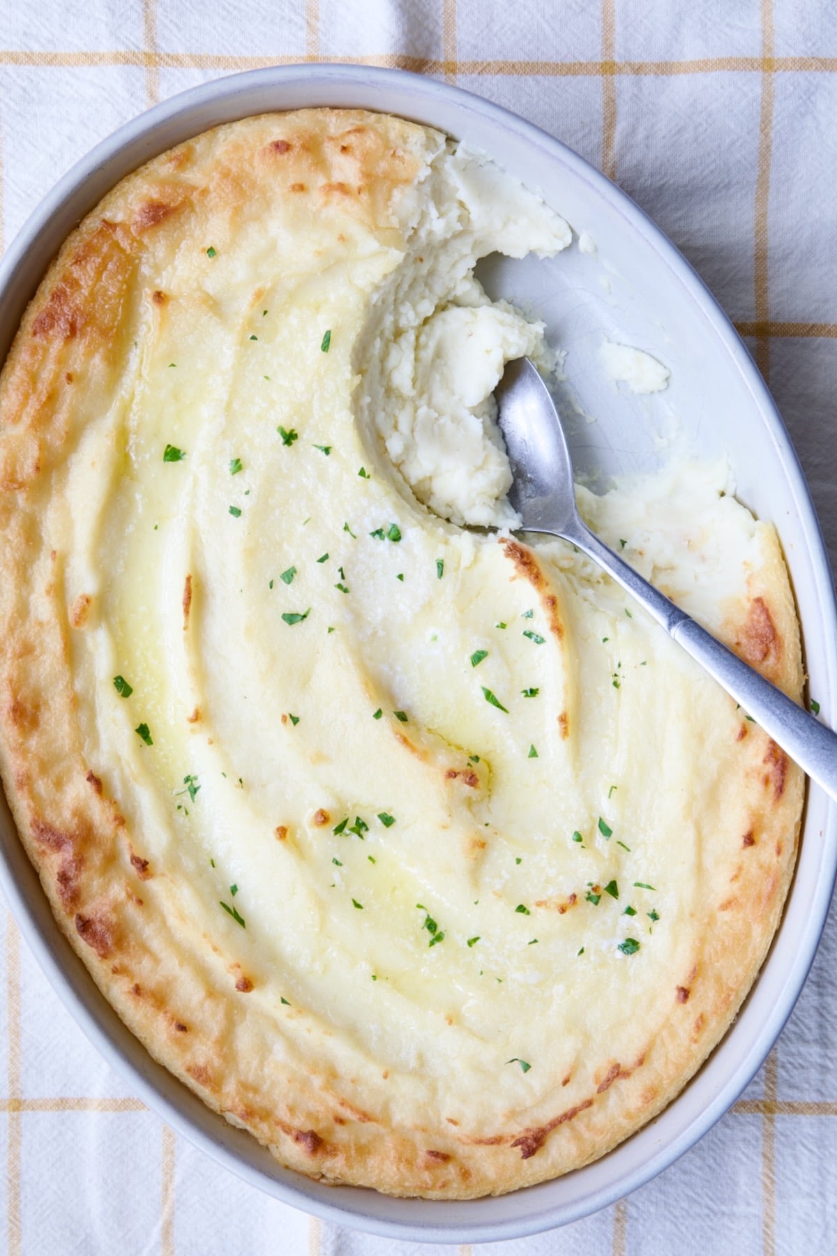 Twice-Baked Mashed Potatoes in white oval baking dish with serving spoon scooping some out.