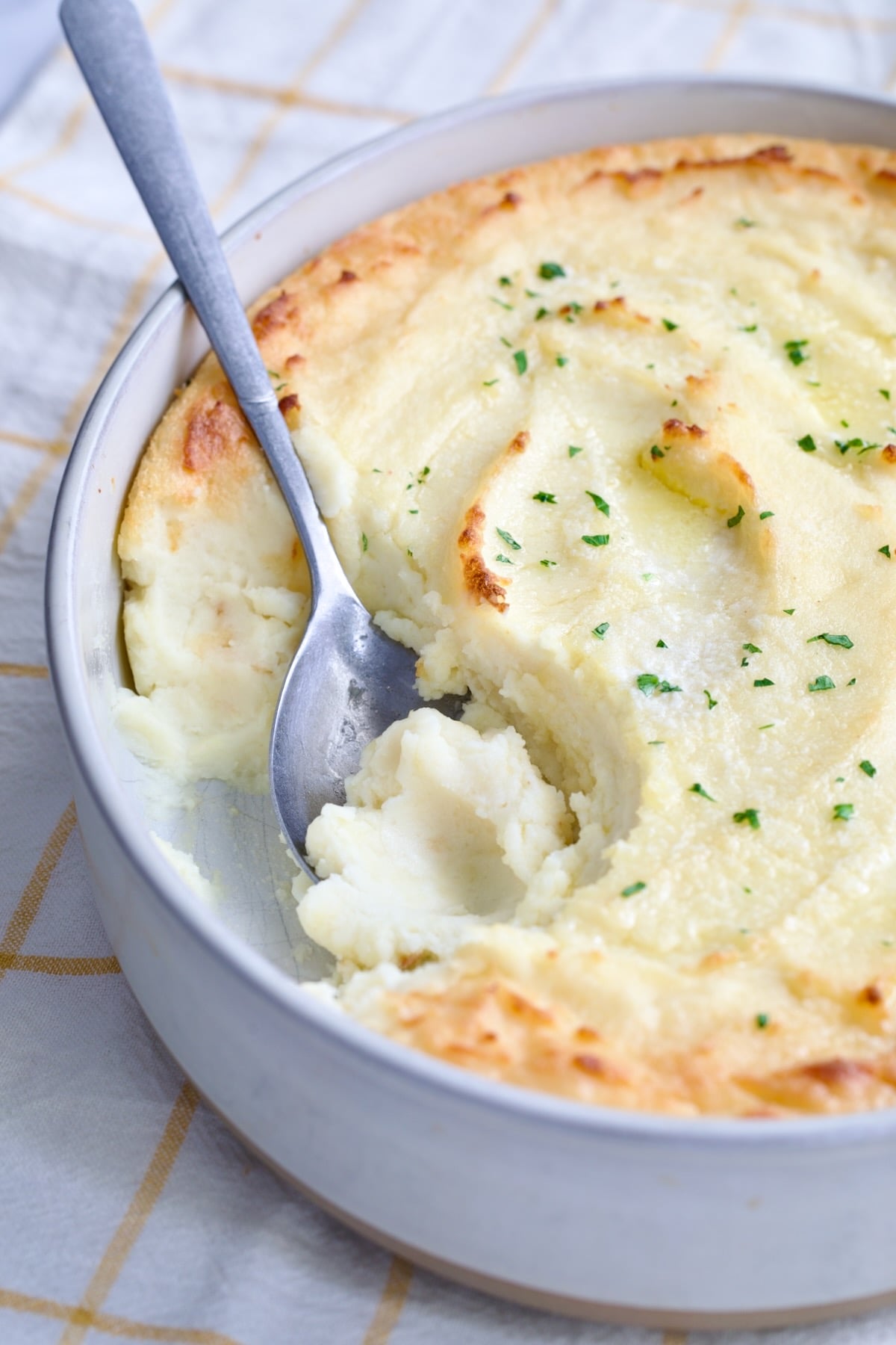 Twice-Baked Mashed Potatoes in white oval baking dish with serving spoon scooping some out.