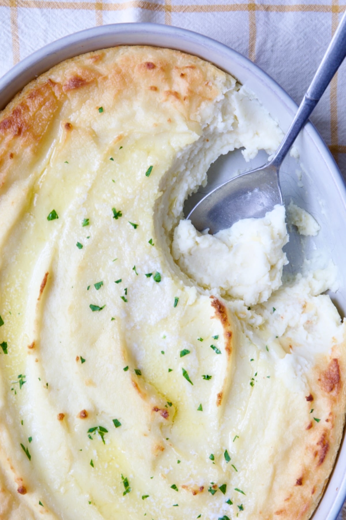 Twice-Baked Mashed Potatoes in white oval baking dish with serving spoon scooping some out.
