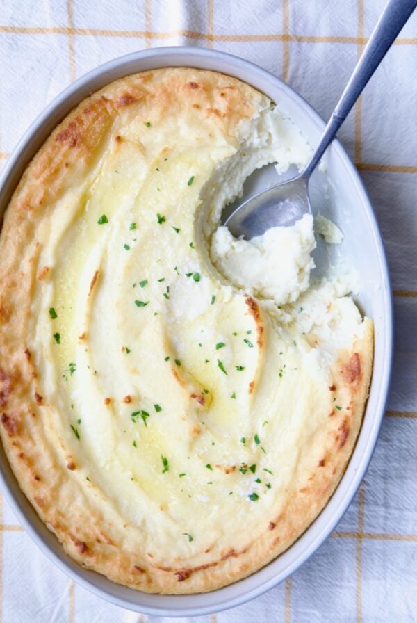 Twice-Baked Mashed Potatoes in white oval baking dish with serving spoon scooping some out.