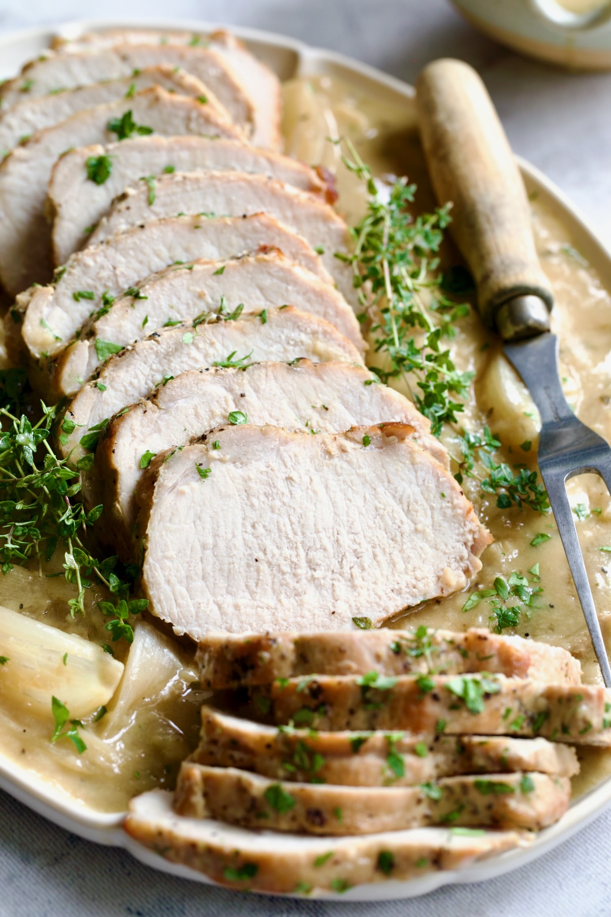 Braised Pork Loin in Dijon Mustard Sauce on a scalloped oval platter with meat fork garnished with thyme sprigs.
