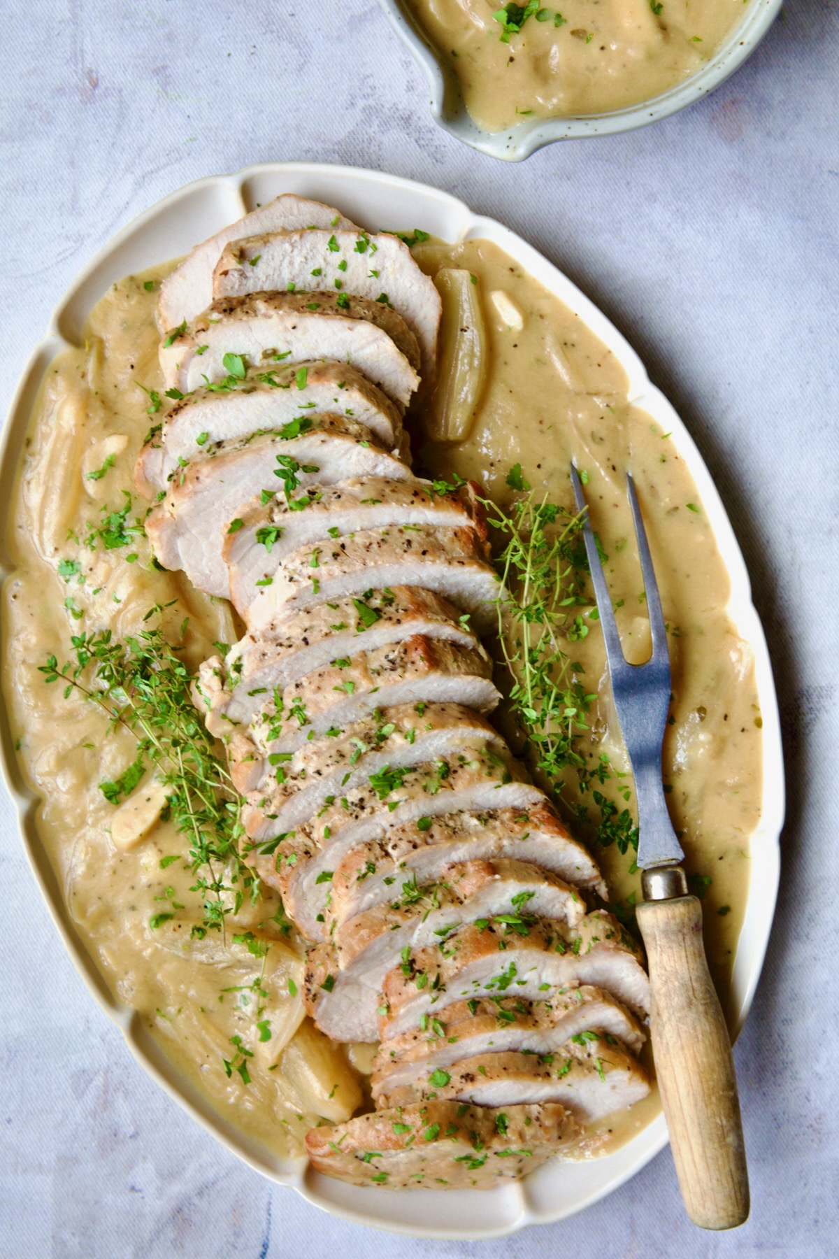 Braised Pork Loin in Dijon Mustard Sauce on a scalloped oval platter garnished with thyme sprigs.