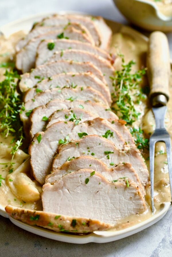 Braised Pork Loin in Dijon Mustard Sauce on a scalloped oval platter with meat fork garnished with thyme sprigs.