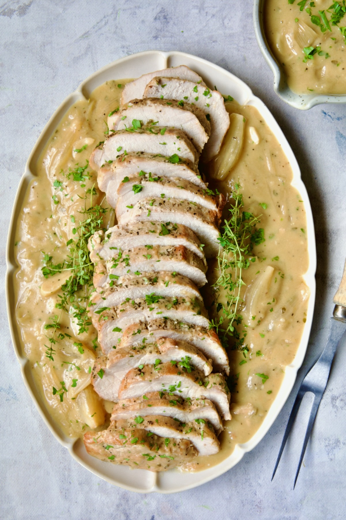 Braised Pork Loin in Dijon Mustard Sauce on a scalloped oval platter garnished with thyme sprigs.
