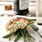 One serving of Crab-Stuffed Chicken Breasts over asparagus on thin piece of marble.