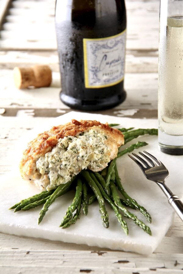 One serving of Crab-Stuffed Chicken Breasts over asparagus on thin piece of marble.