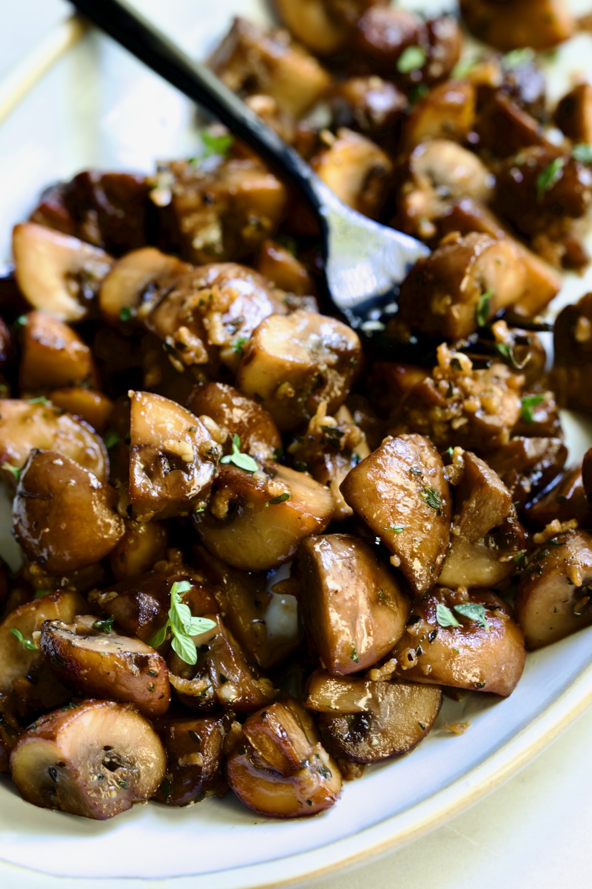 Garlic Butter Mushrooms on oval white platter with black dinner fork garnished with fresh thyme.