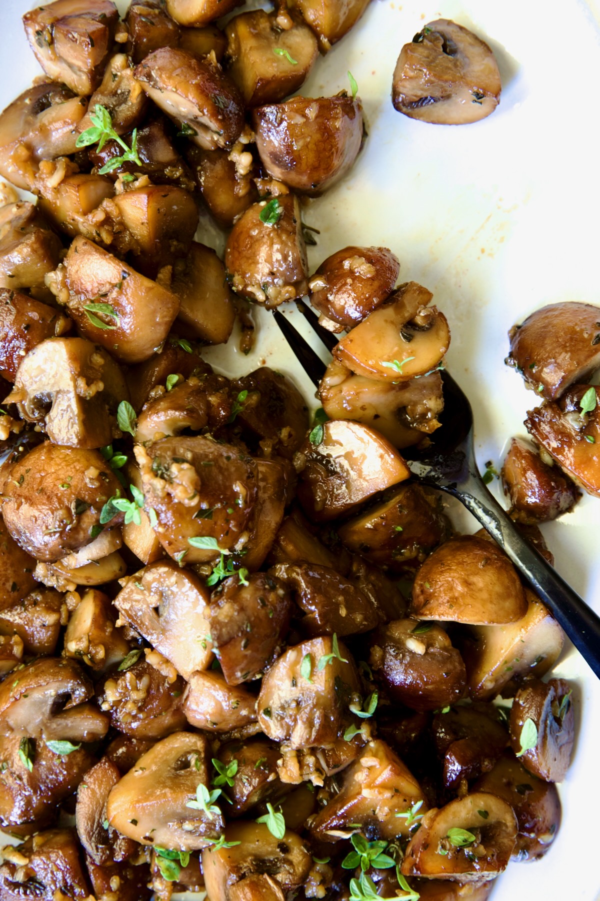 Garlic Butter Mushrooms on oval white platter with black dinner fork.