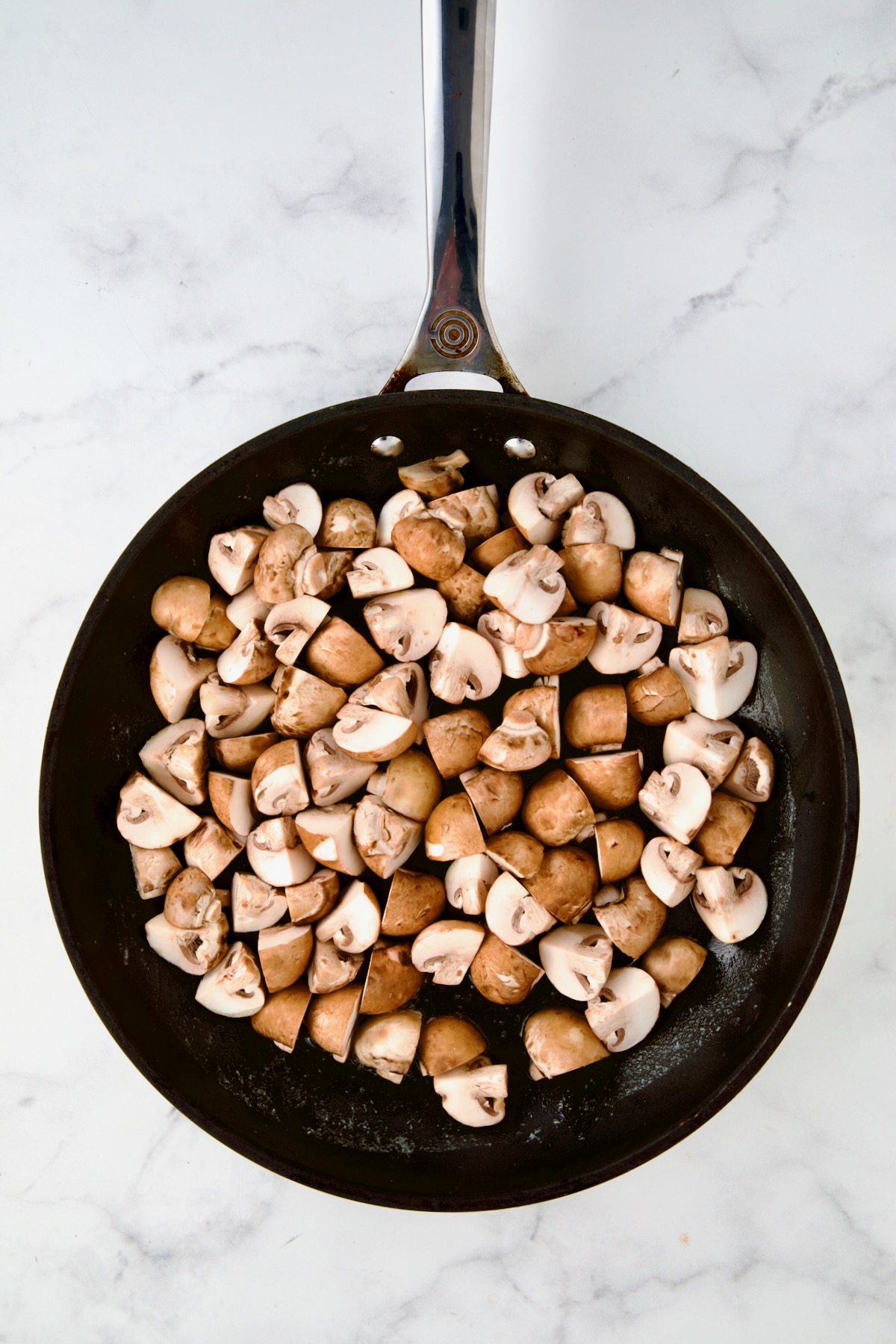 Uncooked cremini mushrooms in nonstick skillet.