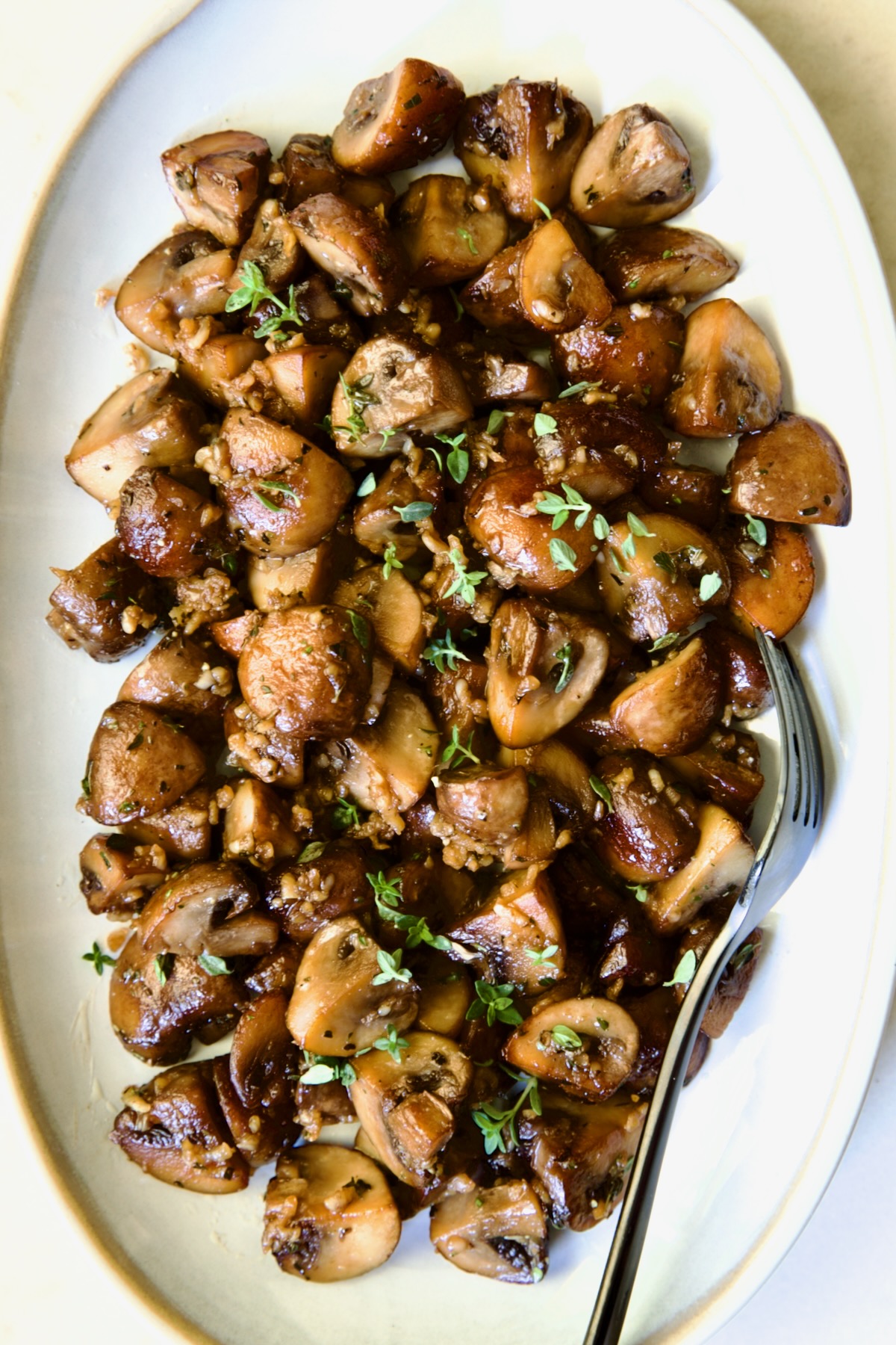 Garlic Butter Mushrooms on oval white platter with black dinner fork.