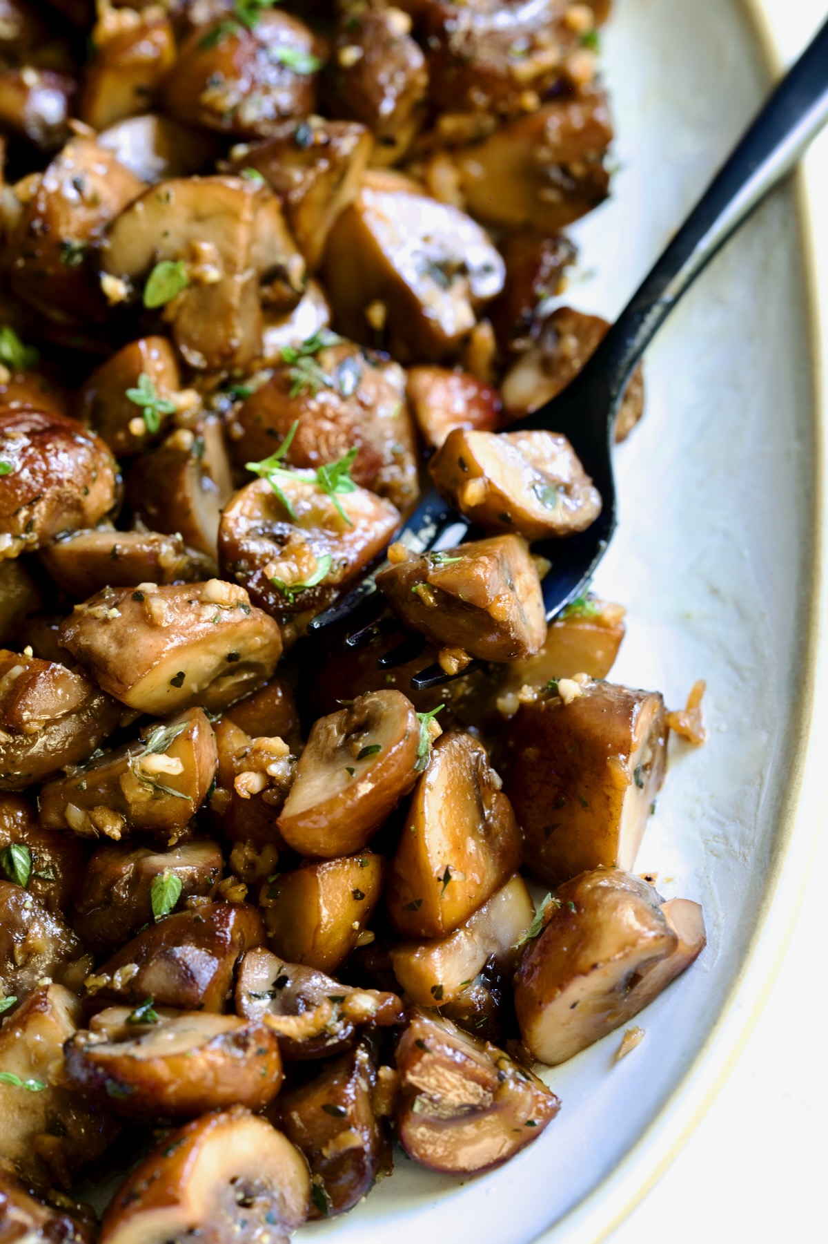 Garlic Butter Mushrooms on oval white platter with black dinner fork.