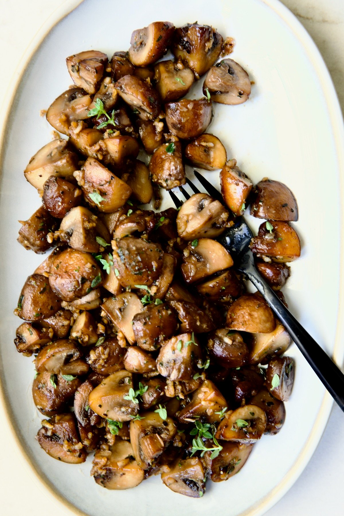 Garlic Butter Mushrooms on oval white platter with black dinner fork.