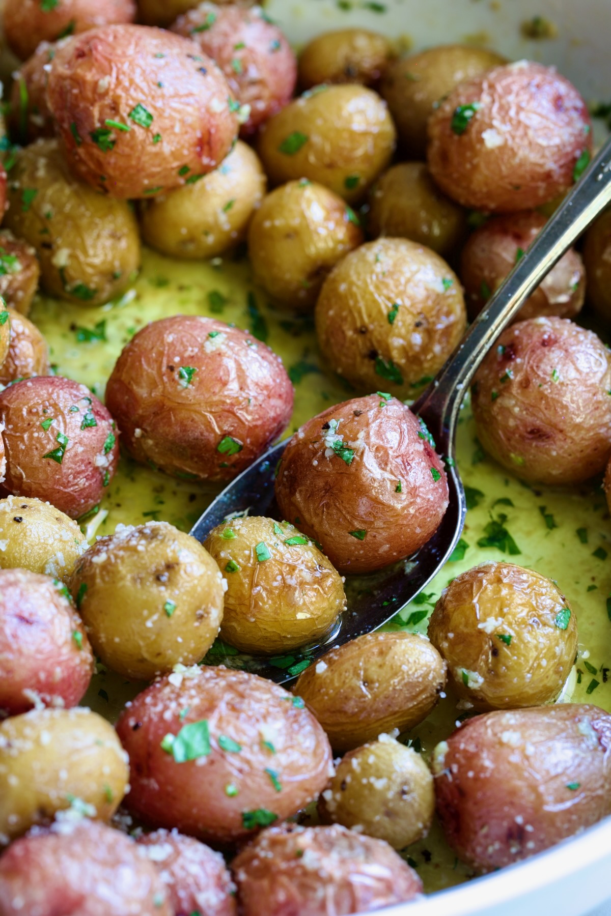 Garlic Butter Parmesan Mini Potatoes in round white baking dish with serving spoon.
