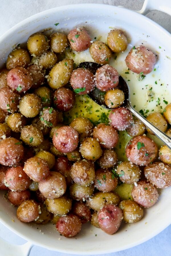 Garlic Butter Parmesan Mini Potatoes in round white baking dish with serving spoon.