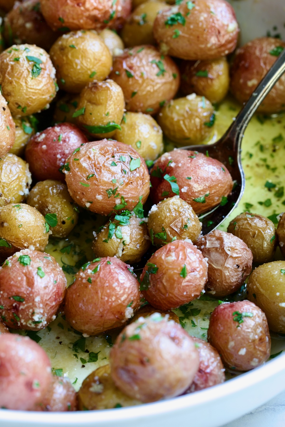 Garlic Butter Parmesan Mini Potatoes in round white baking dish with serving spoon.