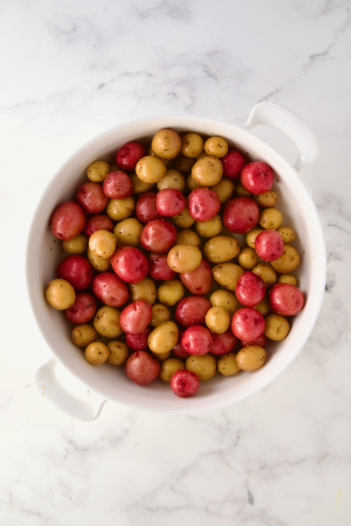 Uncooked mini potatoes in round white baking dish.