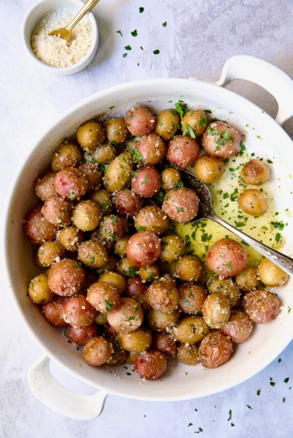 Garlic Butter Parmesan Mini Potatoes in round white baking dish with serving spoon.