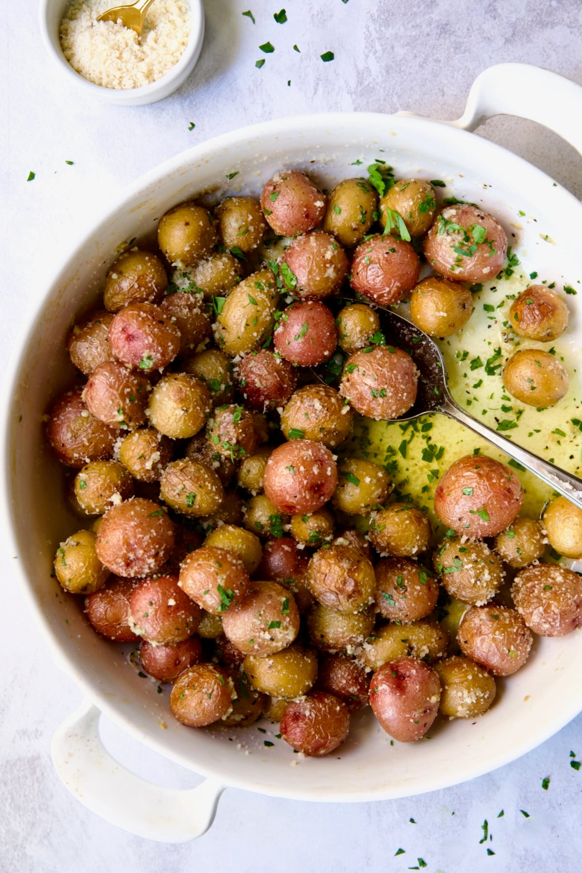 Garlic Butter Parmesan Mini Potatoes in round white baking dish with serving spoon.