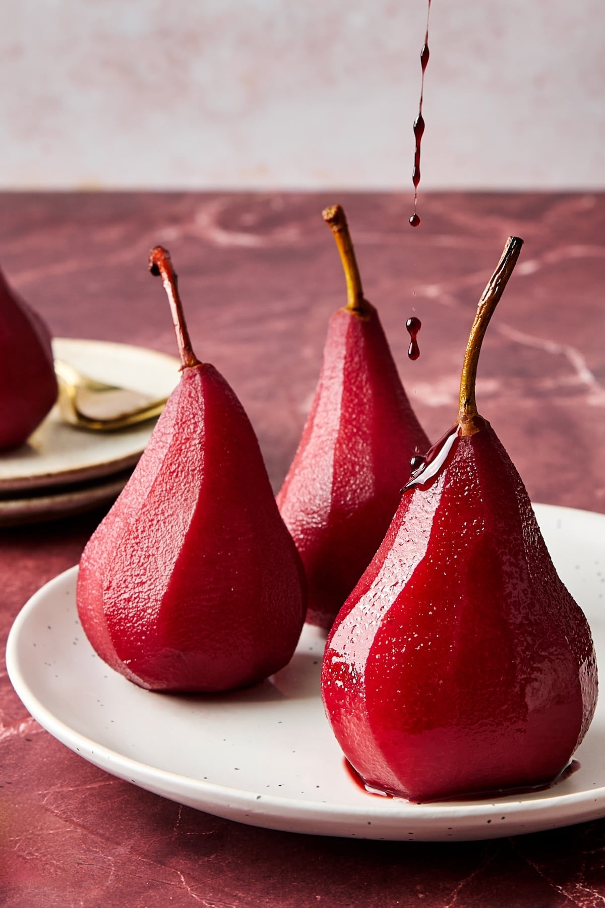 Three poached pears on white plate being drizzled with sauce.