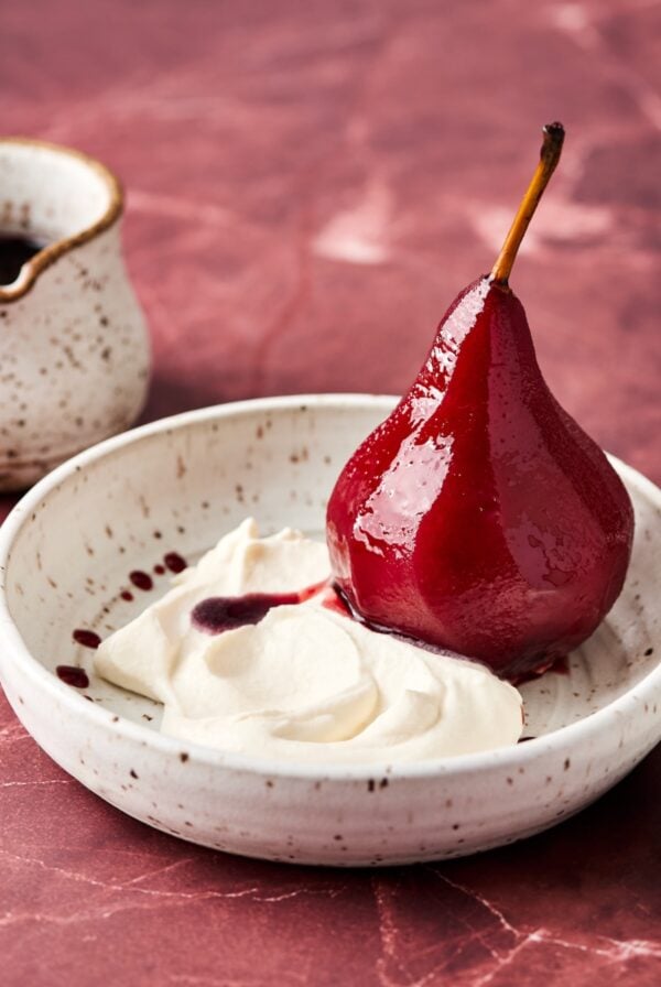 Poached pear sliced in half in bowl with Mascarpone Whipped Cream.