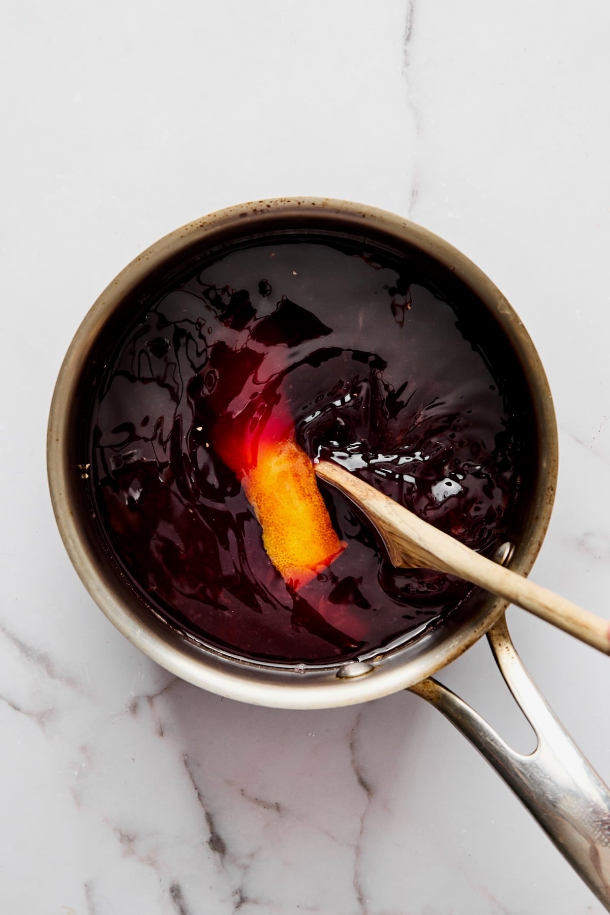 Red wine sauce in stainless steel sauce pan being mixed with wooden spoon.