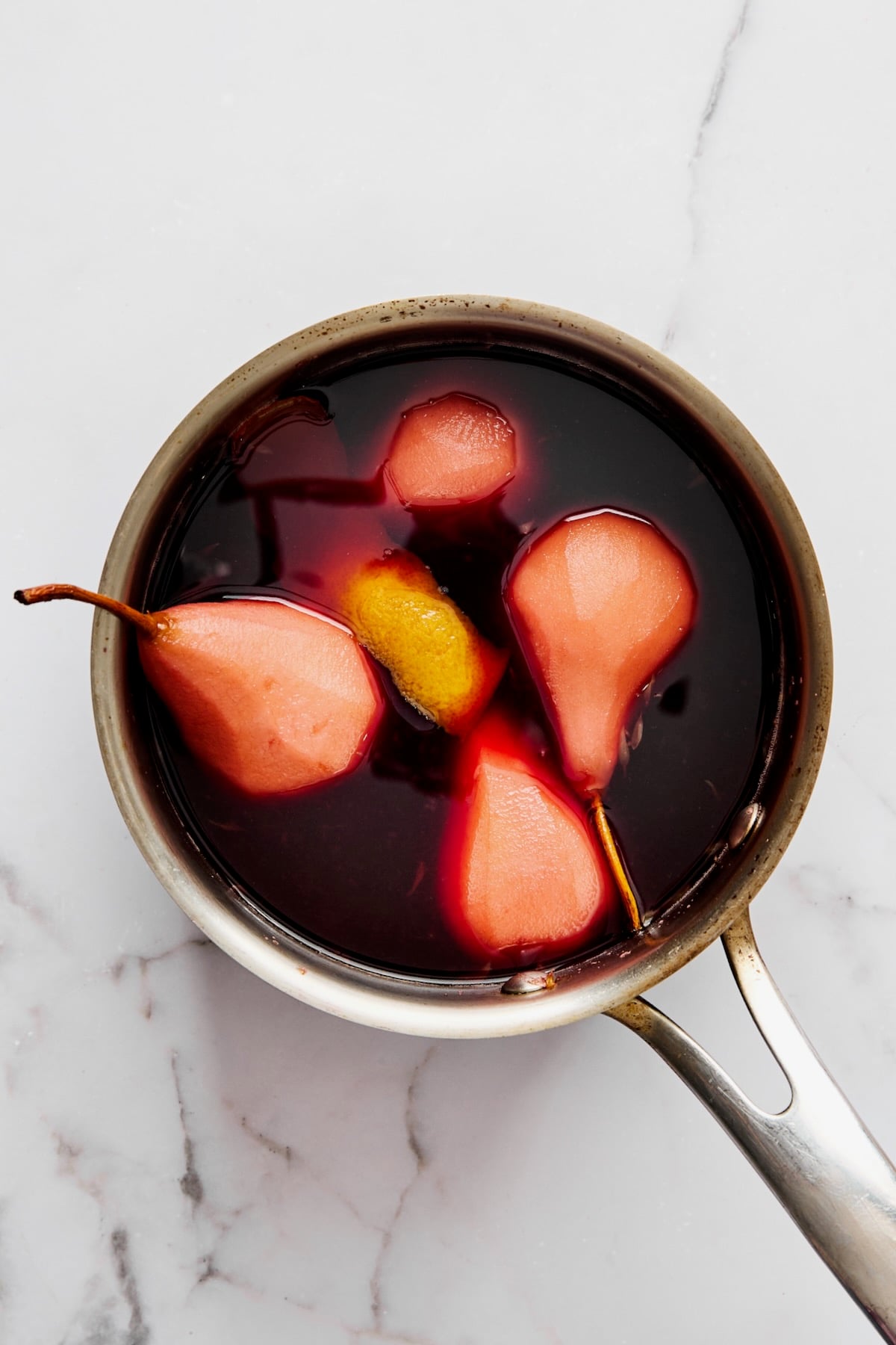 Four simmered pears in red wine sauce in stainless steel saucepan.