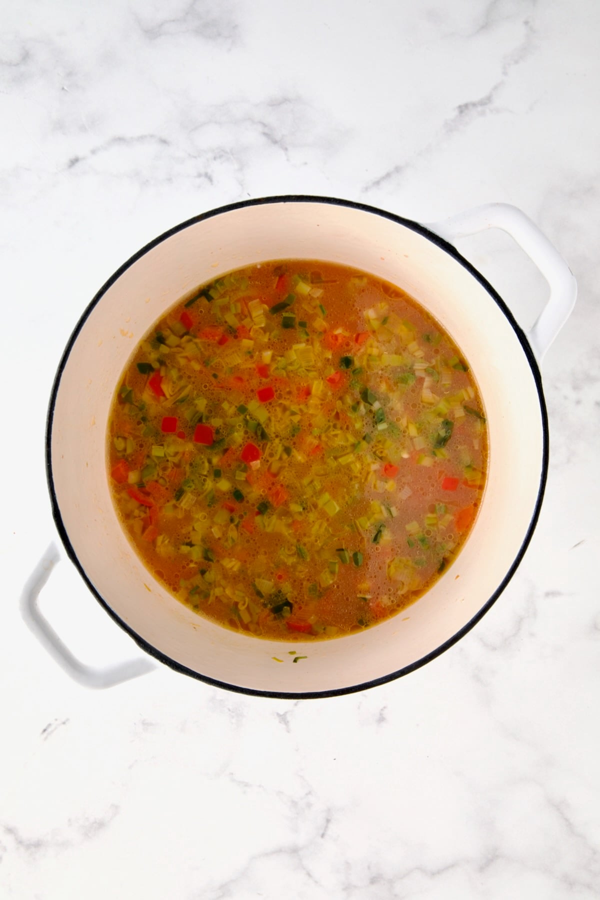 Broth added to vegetables in white Dutch oven.