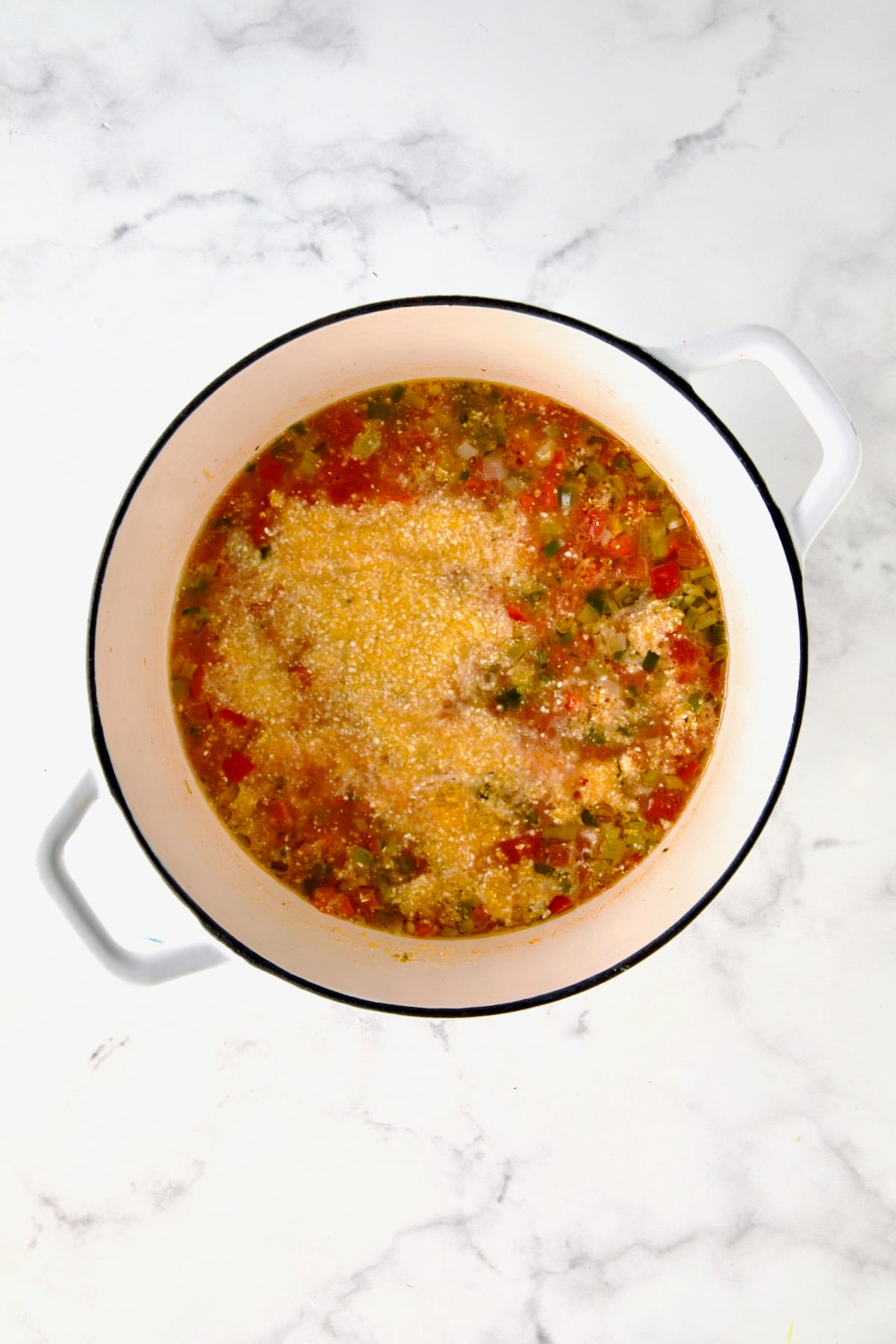 Grits added to vegetables and broth in white Dutch oven before being stirred in.