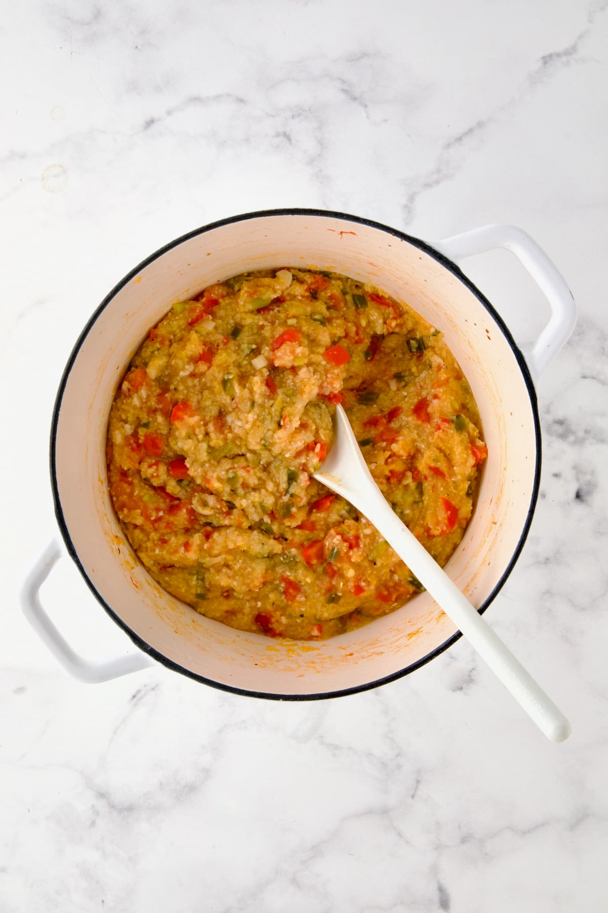 Cooked grits and vegetables in white Dutch oven.