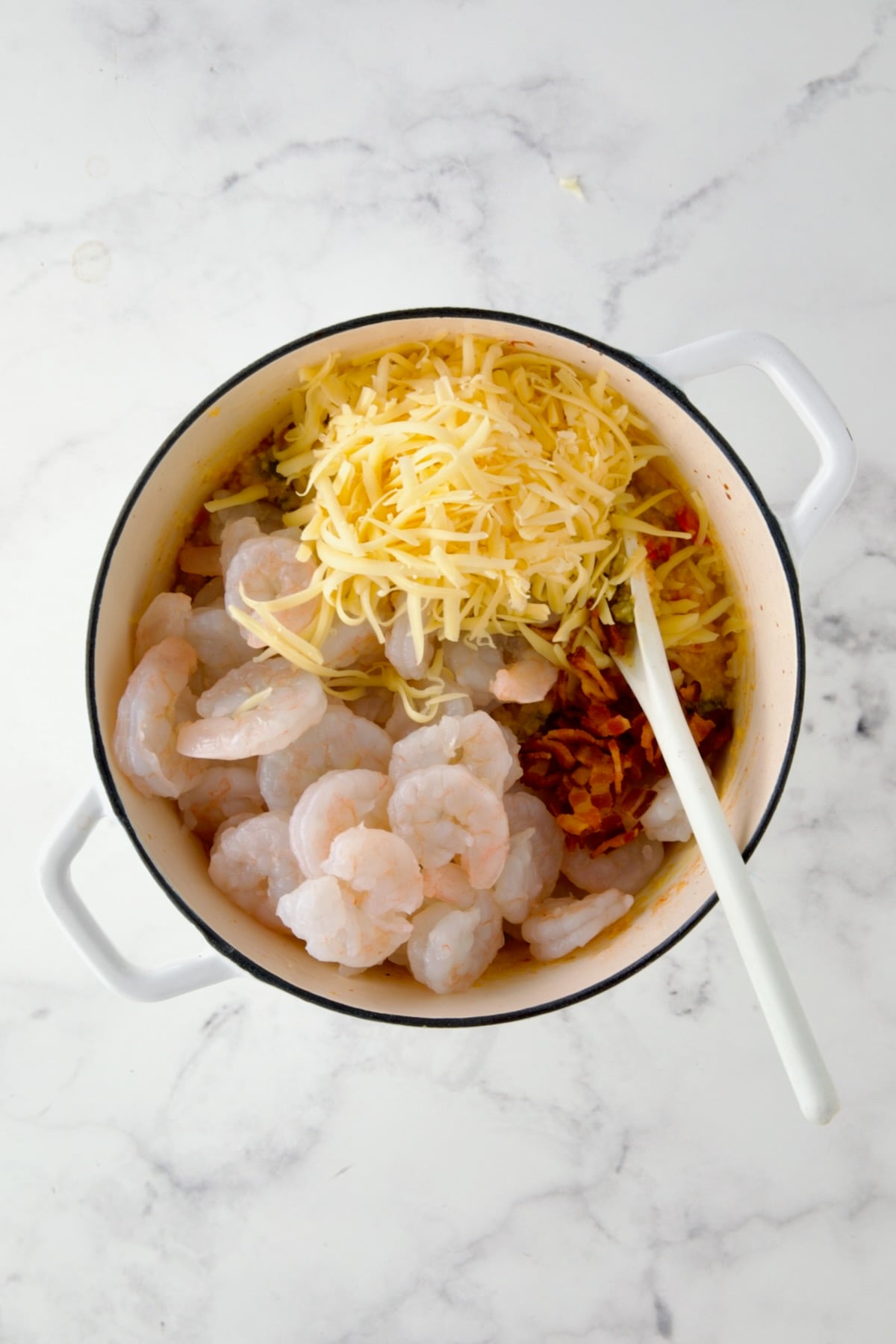 Shrimp and cheese added to vegetable and grits combination in white Dutch oven.