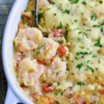 Shrimp and Grits Casserole in oval white baking dish with serving spoon.