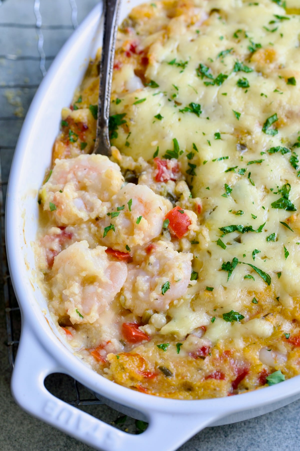 Shrimp and Grits Casserole in oval white baking dish with serving spoon.