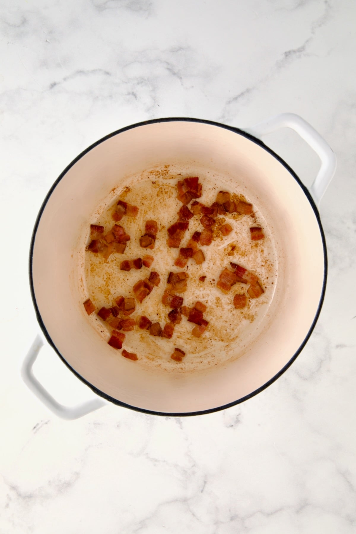 Cooked bacon in white Dutch oven.