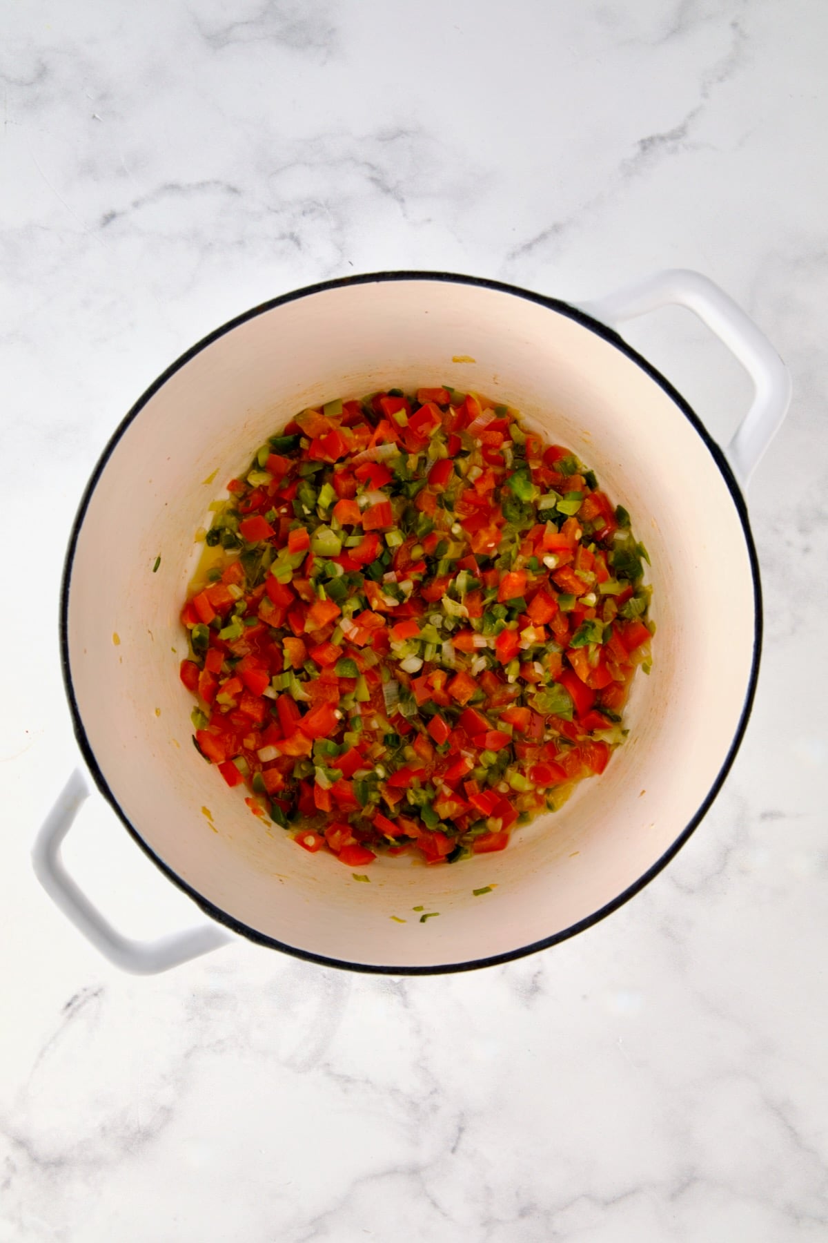 Cooked scallion, jalapeno and red bell pepper in white Dutch oven.