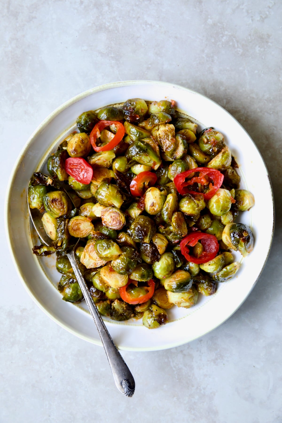 Hot Honey Brussels Sprouts in white serving bowl with serving spoon.
