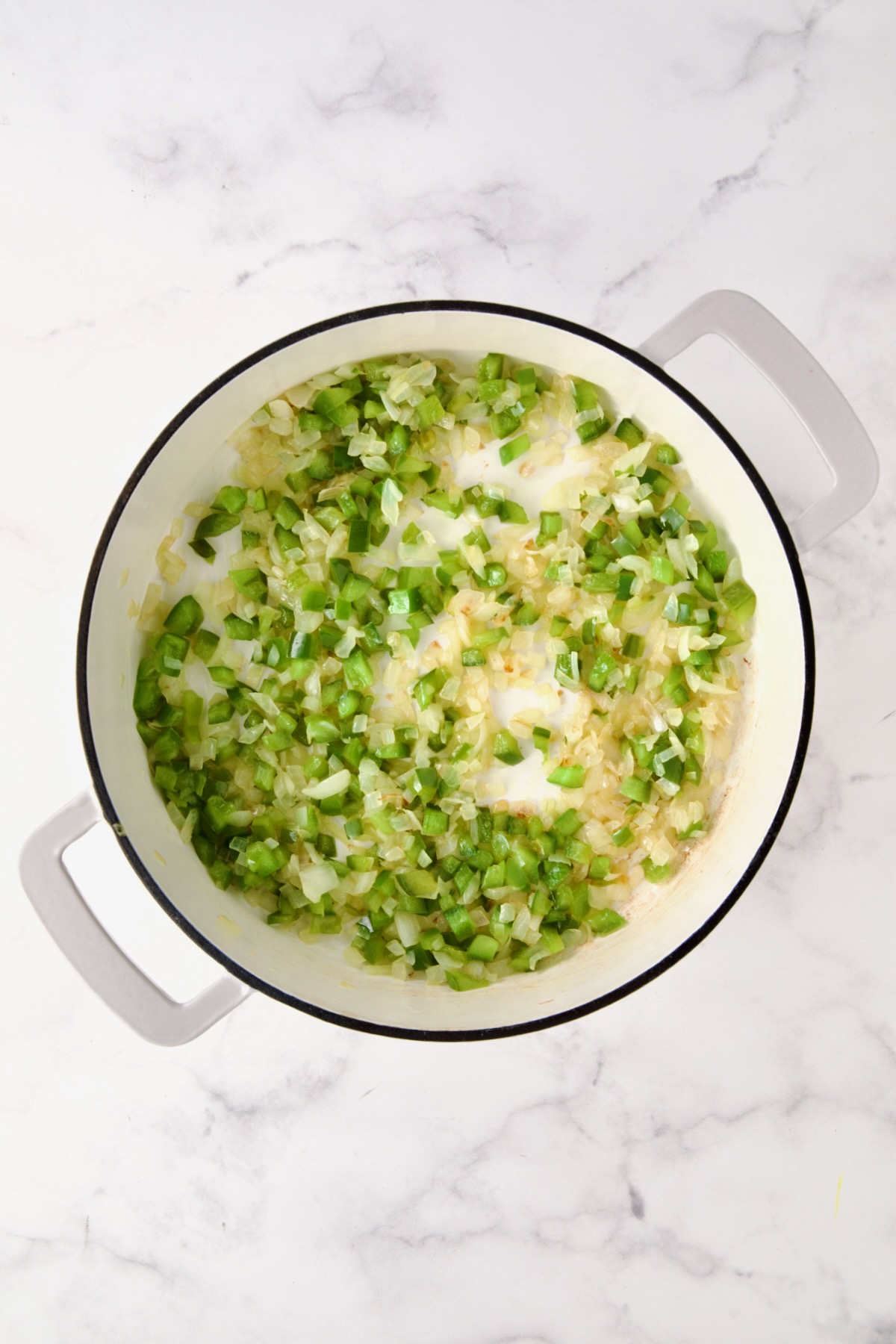 Cooked onions and green bell pepper in white enamel cast iron skillet.
