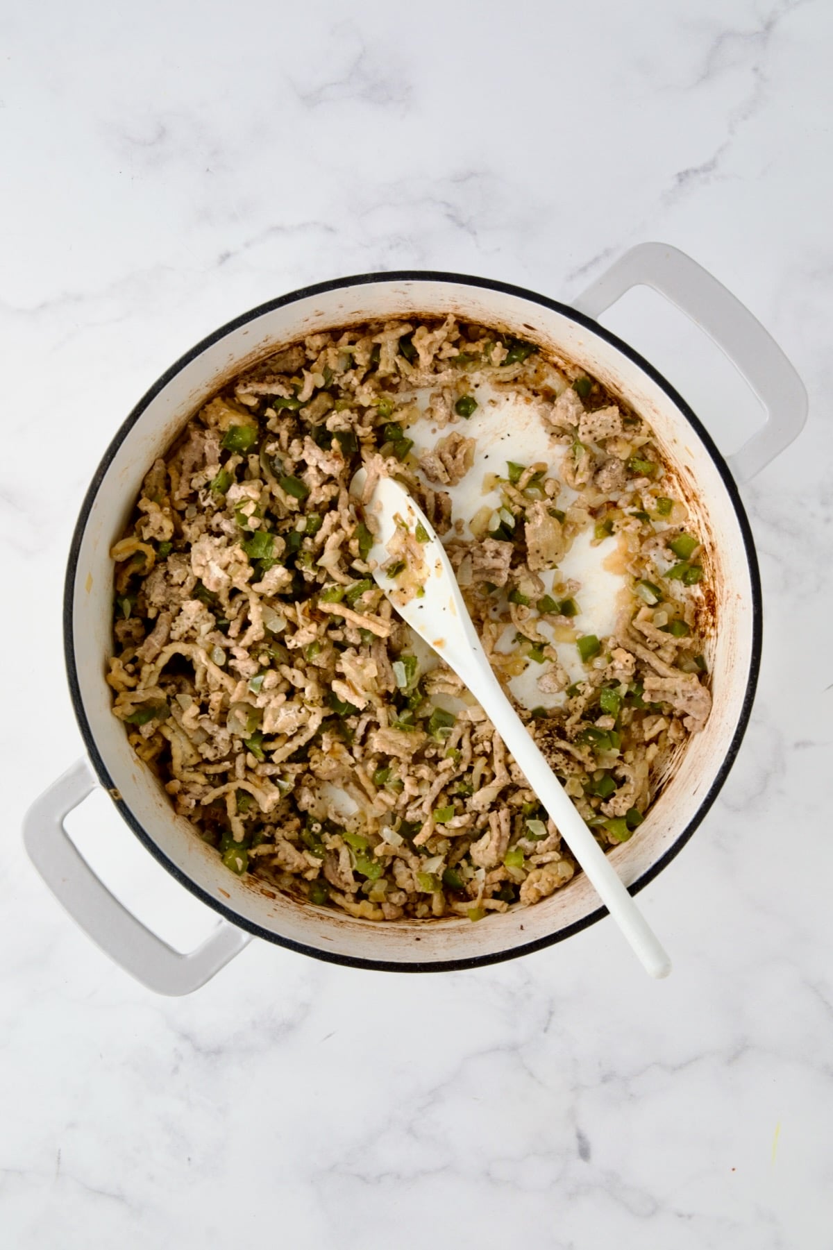 Cooked ground turkey with cooked onions and peppers in white enamel cast iron skillet.