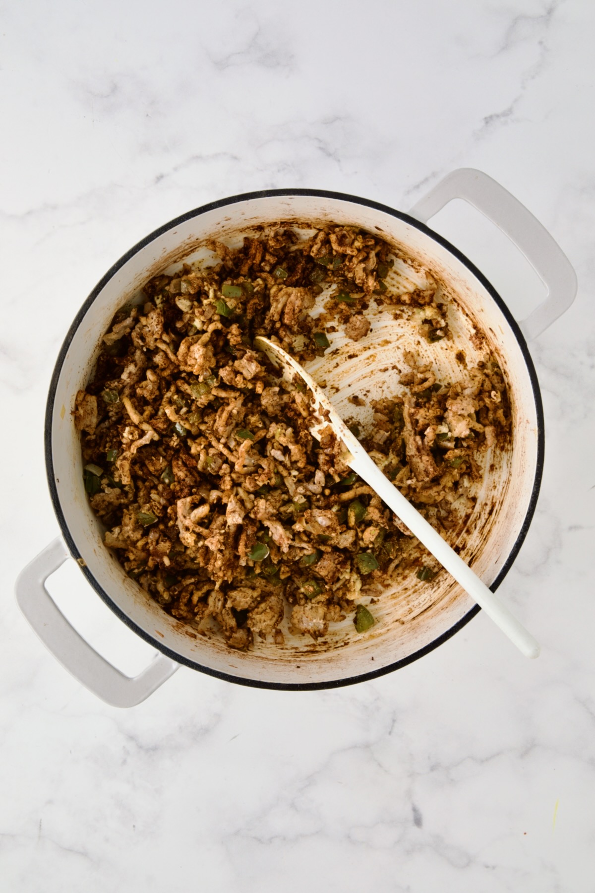 Spices added to ground turkey, peppers and onions in white enamel cast iron skillet.