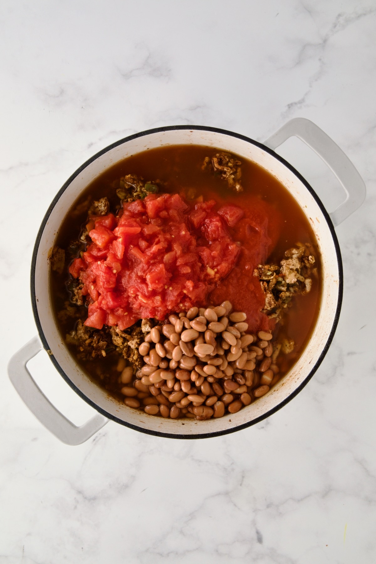 Diced tomatoes, tomato sauce, beans and broth added to ground turkey, onions and green pepper in white enamel cast iron skillet.