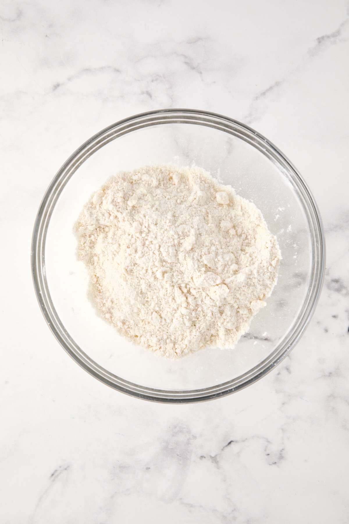 Butter added to dry ingredients in glass bowl.