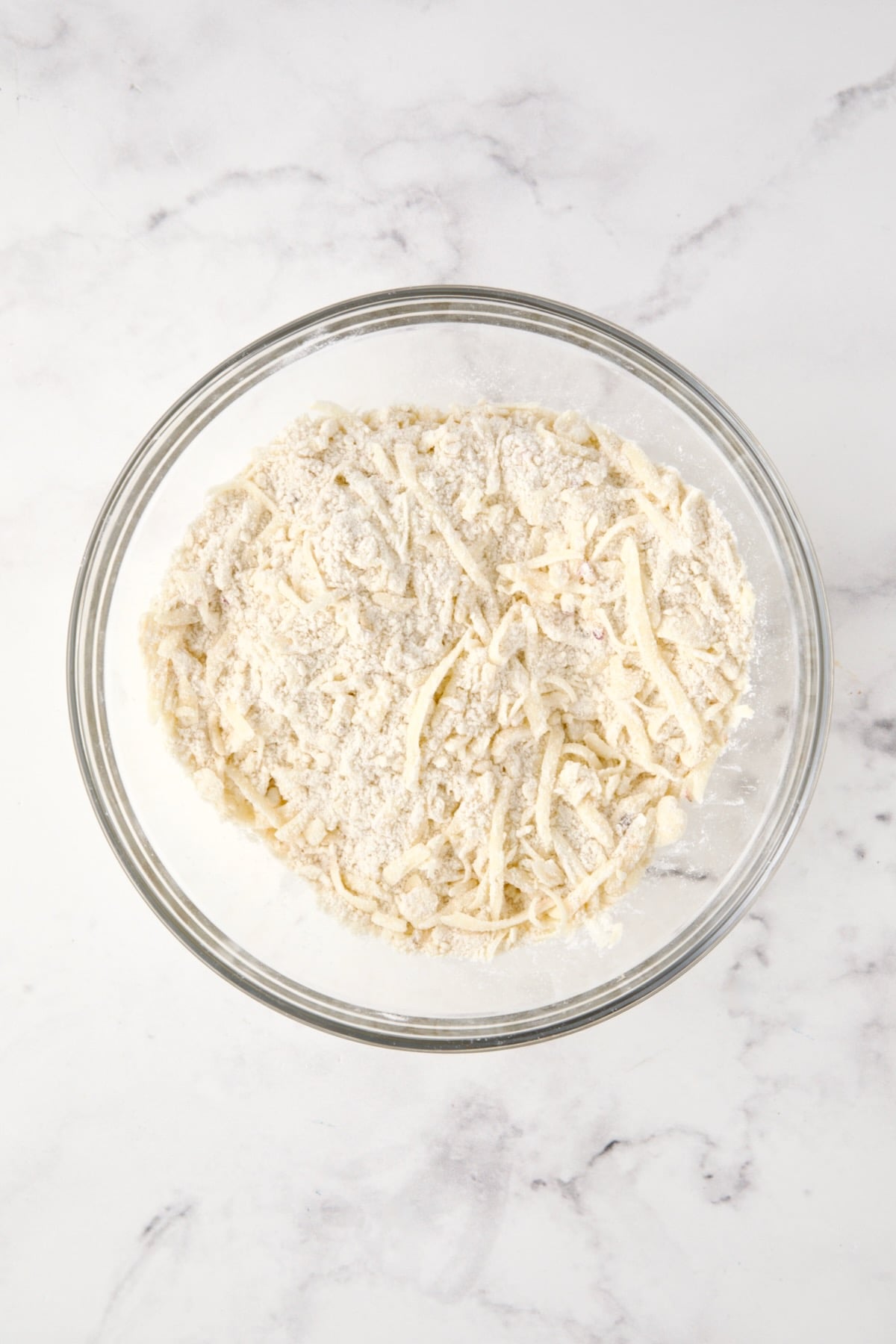 Cheese added to dry ingredients and butter in glass bowl.